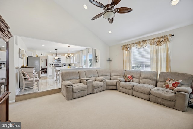 living room featuring a wealth of natural light, light carpet, high vaulted ceiling, and ceiling fan with notable chandelier