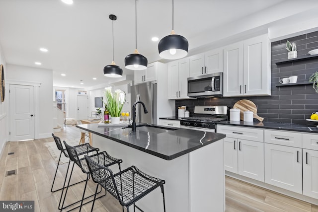 kitchen featuring dark countertops, appliances with stainless steel finishes, a breakfast bar area, white cabinets, and decorative backsplash