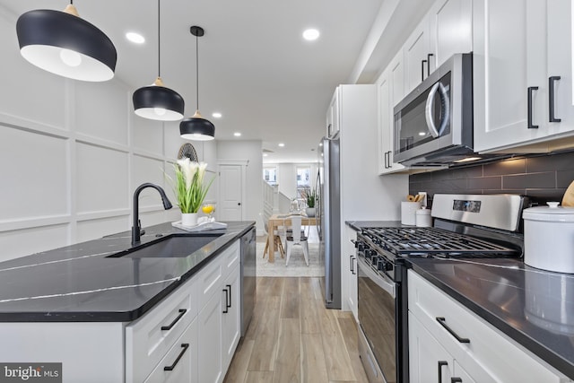 kitchen featuring a sink, light wood-style floors, appliances with stainless steel finishes, a decorative wall, and tasteful backsplash