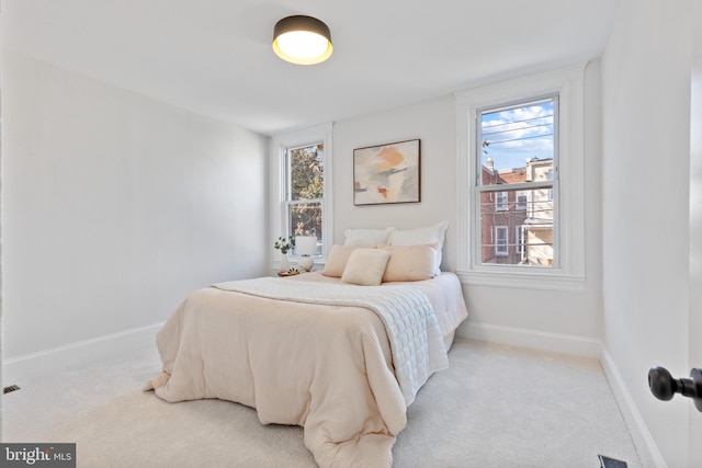 bedroom featuring light carpet, multiple windows, and baseboards