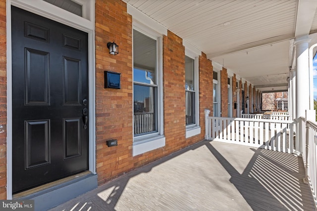 view of exterior entry featuring a porch and brick siding