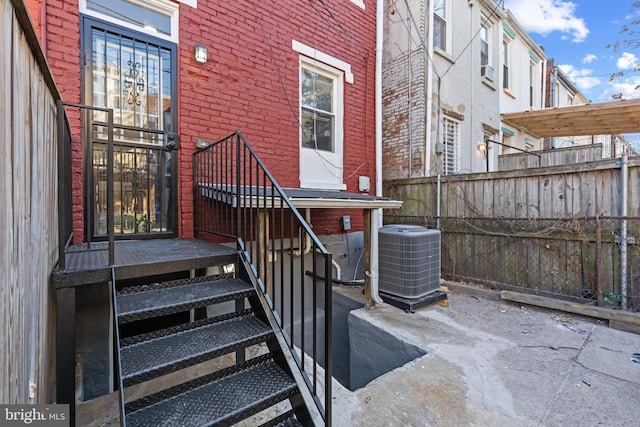 property entrance featuring cooling unit, fence, and brick siding