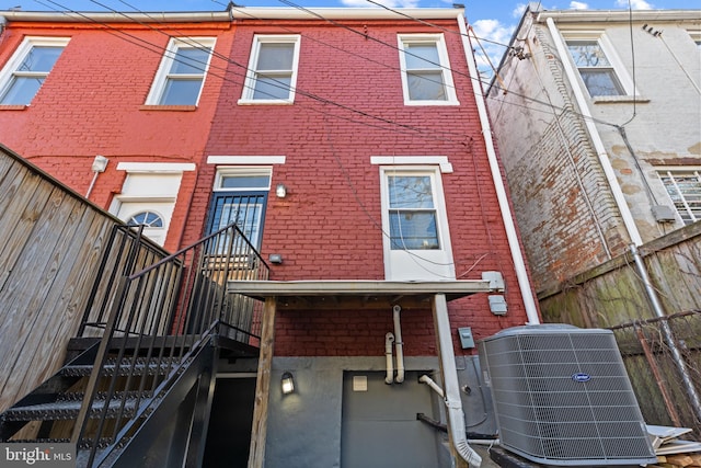 back of house with brick siding, central AC unit, and fence