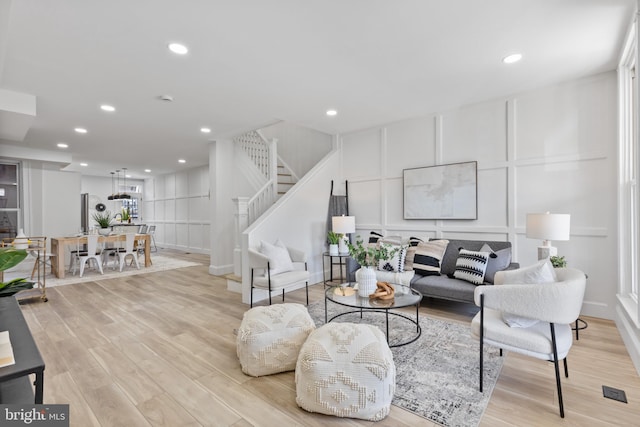 living area with light wood finished floors, a decorative wall, recessed lighting, and stairway