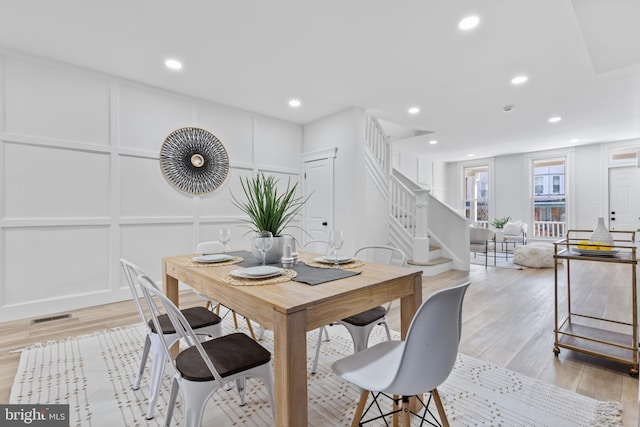 dining room with visible vents, light wood finished floors, stairs, and a decorative wall