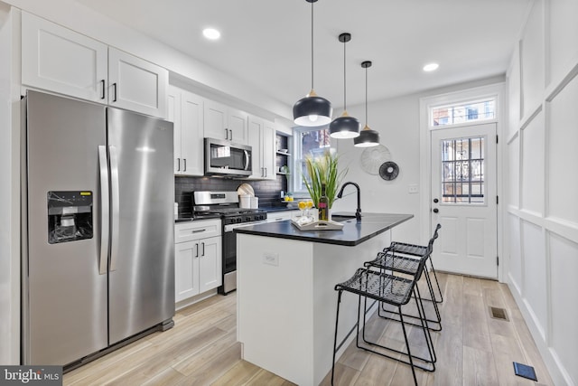 kitchen with visible vents, stainless steel appliances, dark countertops, a kitchen breakfast bar, and backsplash