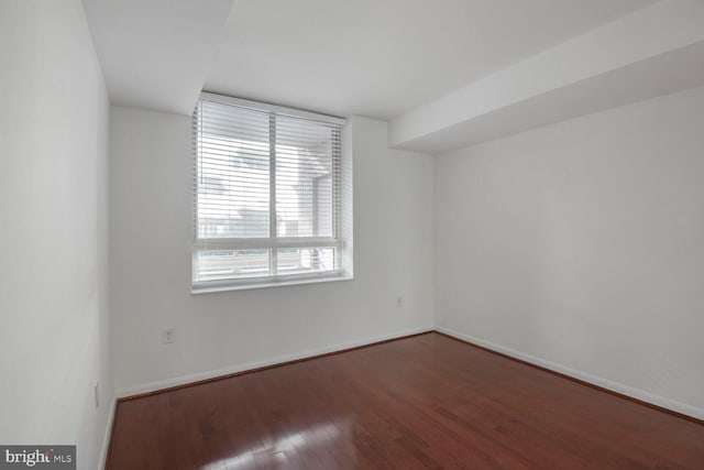 spare room with baseboards and wood finished floors