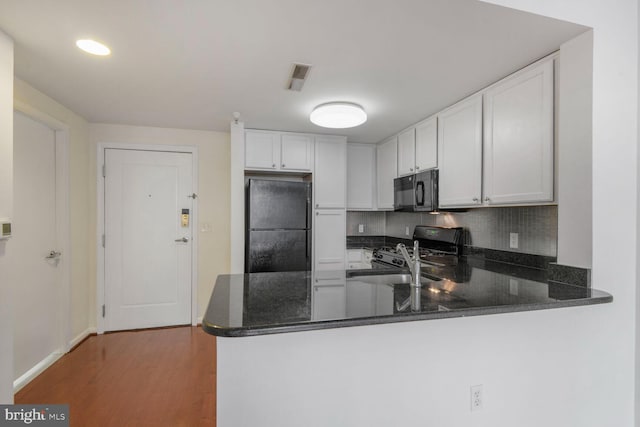 kitchen featuring tasteful backsplash, black appliances, a peninsula, wood finished floors, and white cabinetry