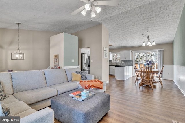 living room with wainscoting, ceiling fan with notable chandelier, a textured ceiling, and wood finished floors