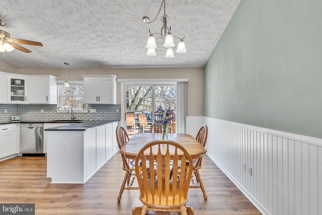 dining space featuring a textured ceiling, a healthy amount of sunlight, wood finished floors, and wainscoting