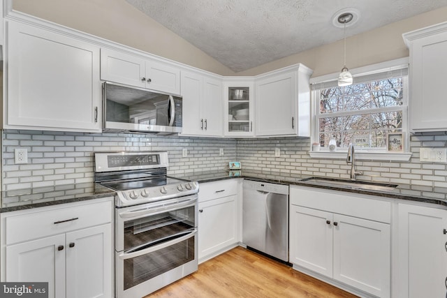 kitchen with vaulted ceiling, light wood-style flooring, appliances with stainless steel finishes, white cabinetry, and a sink