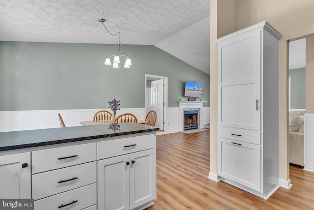 kitchen with a wainscoted wall, light wood-style flooring, dark countertops, white cabinets, and a tile fireplace