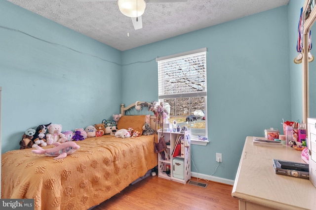 bedroom with visible vents, baseboards, wood finished floors, a textured ceiling, and a ceiling fan