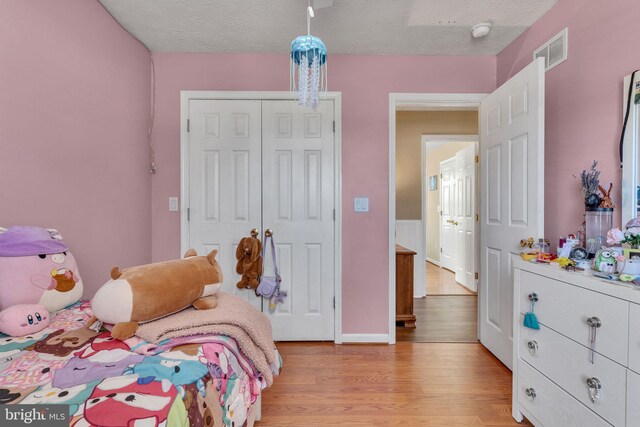 bedroom featuring light wood-style flooring, visible vents, a closet, and a textured ceiling