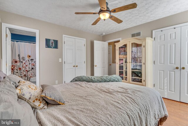 bedroom with visible vents, multiple closets, light wood-style floors, and a textured ceiling