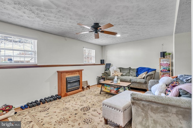 living area with wood finished floors, baseboards, ceiling fan, a textured ceiling, and a glass covered fireplace