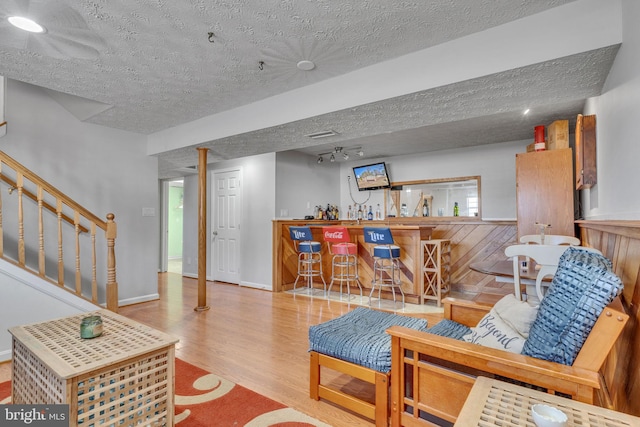 living room featuring baseboards, stairway, wood finished floors, a textured ceiling, and a bar