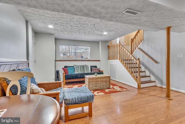 living area with visible vents, baseboards, stairs, wood finished floors, and a textured ceiling