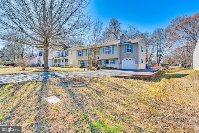 rear view of house with a yard, an attached garage, concrete driveway, and a chimney