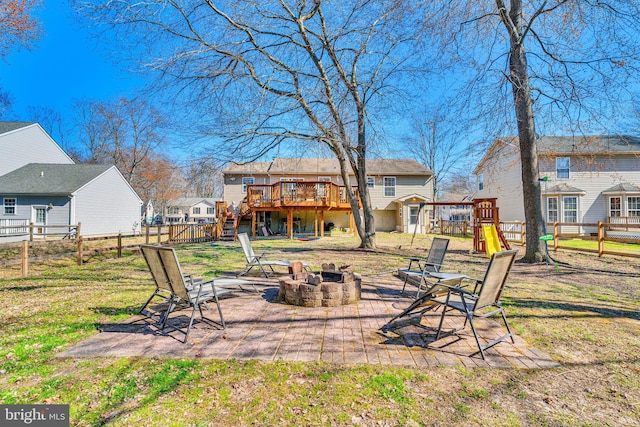 back of house with fence, a wooden deck, a fire pit, a playground, and a lawn