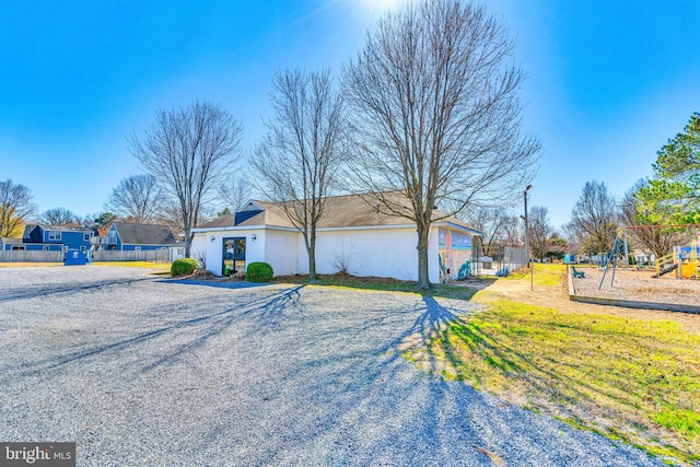 view of front facade with playground community, gravel driveway, stucco siding, and fence