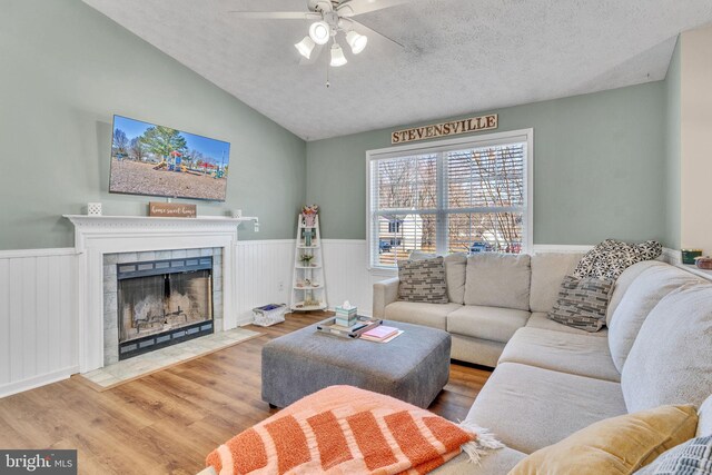 living room with a wainscoted wall, a fireplace, a textured ceiling, and wood finished floors