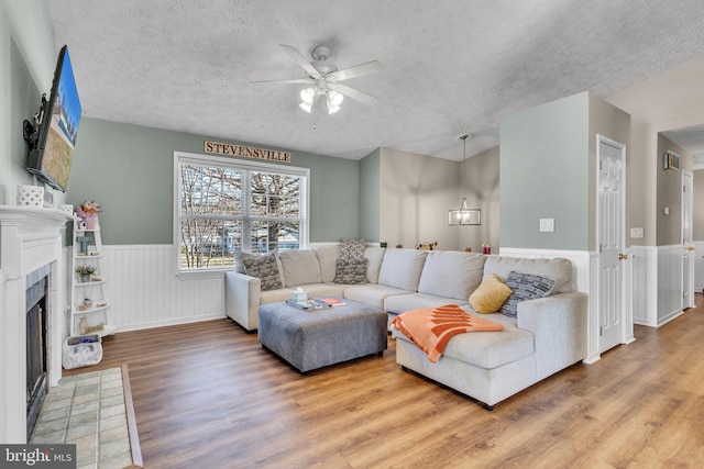 living area featuring wood finished floors, a wainscoted wall, ceiling fan, a textured ceiling, and a tiled fireplace