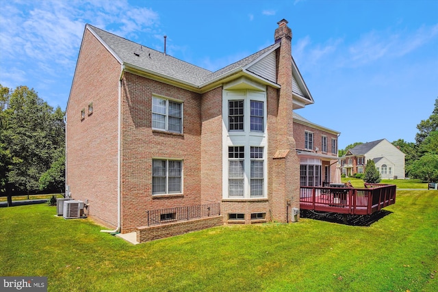 rear view of house with central AC unit, a wooden deck, a chimney, a lawn, and brick siding