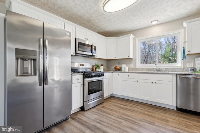 kitchen featuring light wood finished floors, white cabinets, stainless steel appliances, and a sink