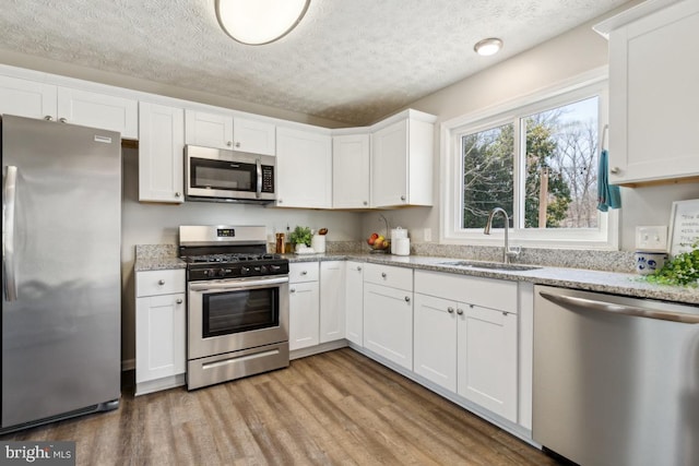 kitchen featuring a sink, white cabinets, light wood-style floors, appliances with stainless steel finishes, and a textured ceiling