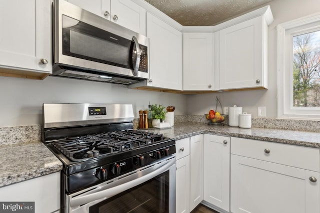 kitchen featuring light stone counters, stainless steel appliances, a textured ceiling, and white cabinets