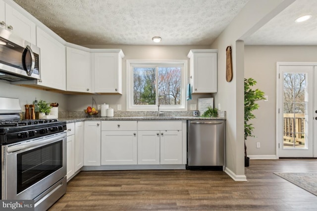 kitchen with a sink, white cabinetry, appliances with stainless steel finishes, baseboards, and dark wood-style flooring