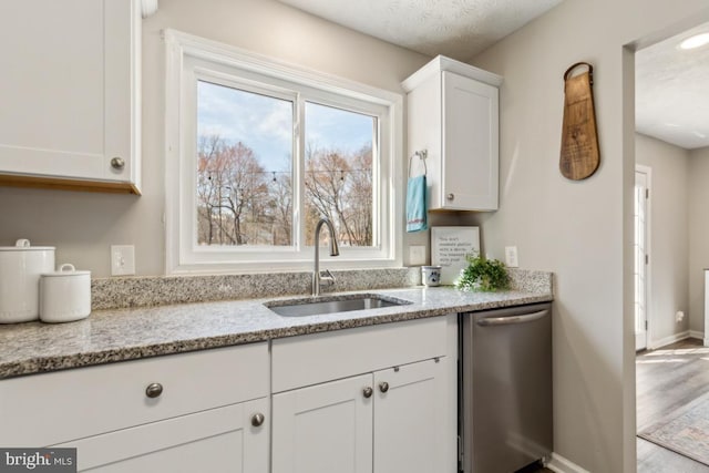 kitchen with a sink, light stone countertops, stainless steel dishwasher, and white cabinets