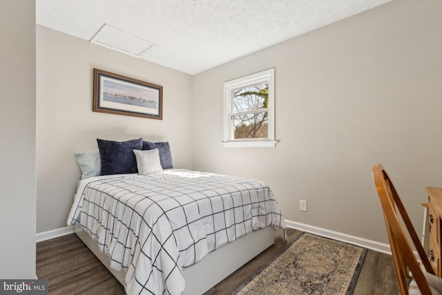 bedroom with baseboards, a textured ceiling, attic access, and wood finished floors