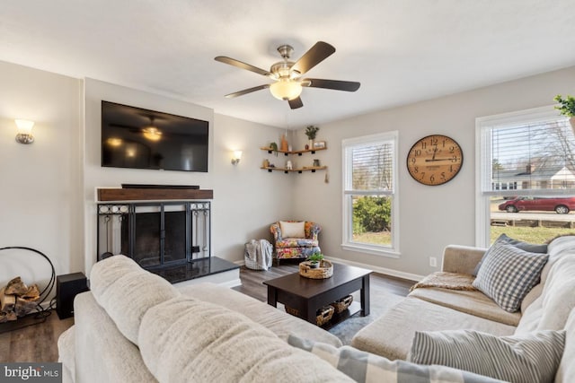 living room with a fireplace with raised hearth, baseboards, a ceiling fan, and wood finished floors