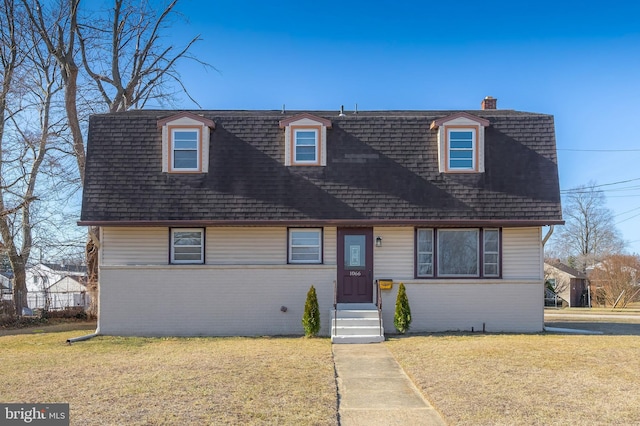 view of front of home featuring brick siding, a chimney, a front yard, and a shingled roof