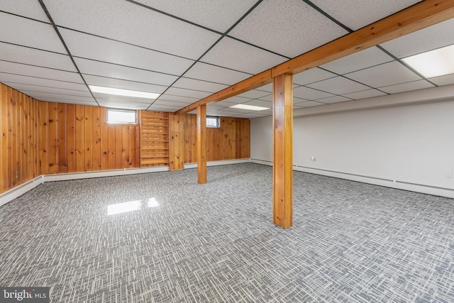 below grade area featuring a drop ceiling, baseboard heating, wood walls, and carpet flooring