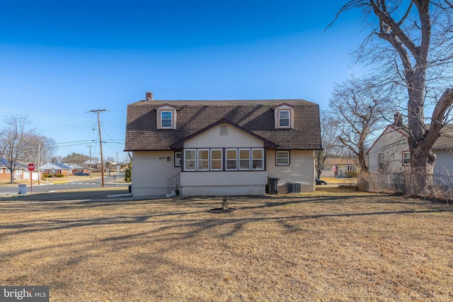 rear view of house with central air condition unit, a lawn, a chimney, and roof with shingles