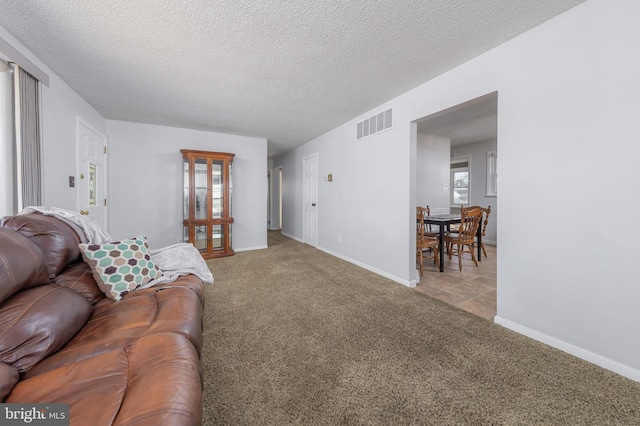 carpeted living room featuring baseboards, visible vents, and a textured ceiling