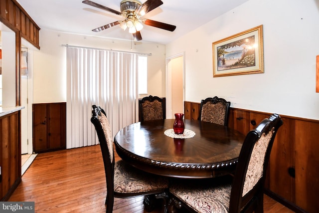 dining space featuring wooden walls, ceiling fan, light wood-type flooring, and wainscoting