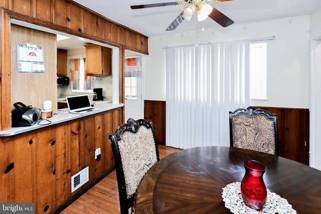 dining area with light wood-type flooring, a wainscoted wall, wood walls, visible vents, and ceiling fan