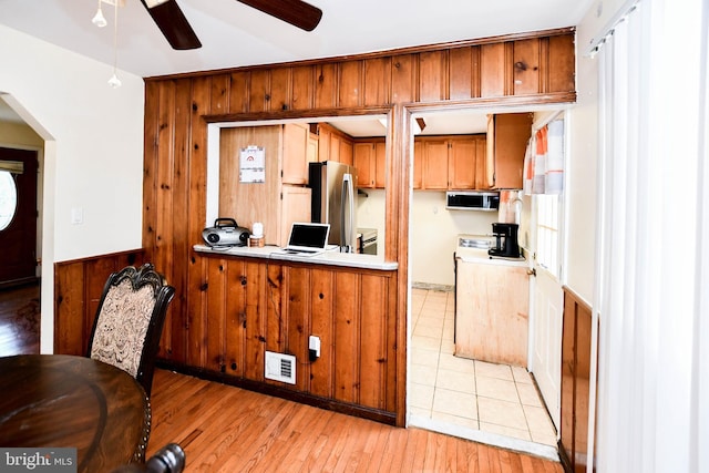 kitchen featuring light wood-type flooring, a peninsula, a ceiling fan, wood walls, and brown cabinets