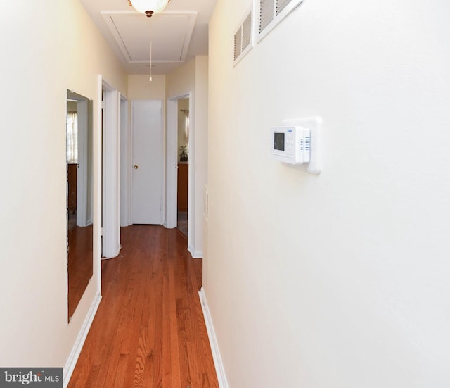 hallway with visible vents, baseboards, attic access, and wood finished floors
