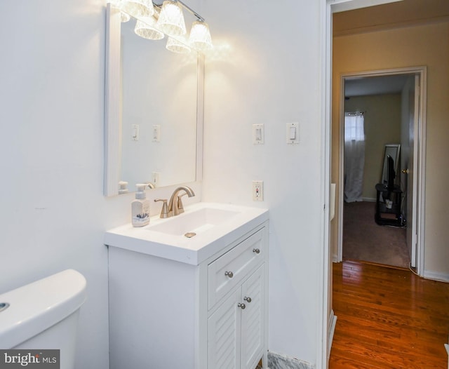 half bath with toilet, vanity, and wood finished floors