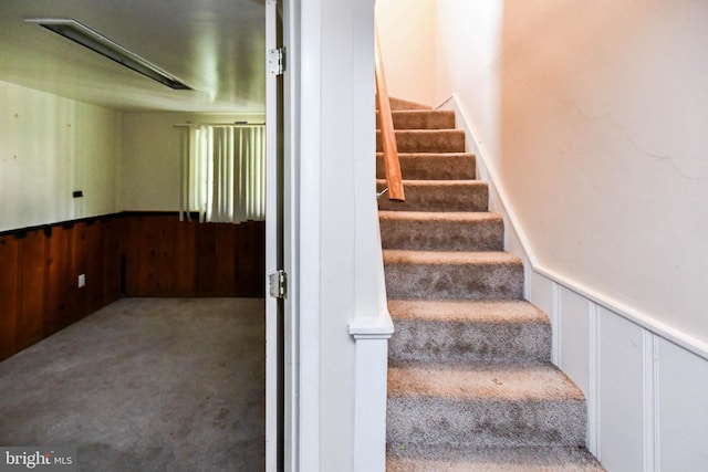 stairs featuring wainscoting and carpet