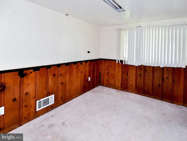 carpeted empty room featuring visible vents, wainscoting, and wood walls