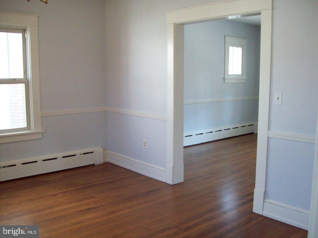 empty room with a baseboard heating unit, plenty of natural light, and dark wood finished floors