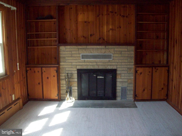 unfurnished living room with wooden walls, visible vents, carpet floors, a fireplace, and a baseboard radiator