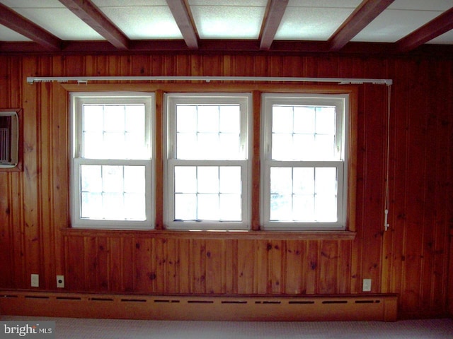 interior space featuring beam ceiling, carpet, and wood walls