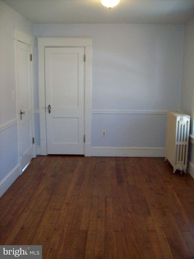 unfurnished room with baseboards, hardwood / wood-style floors, and radiator heating unit